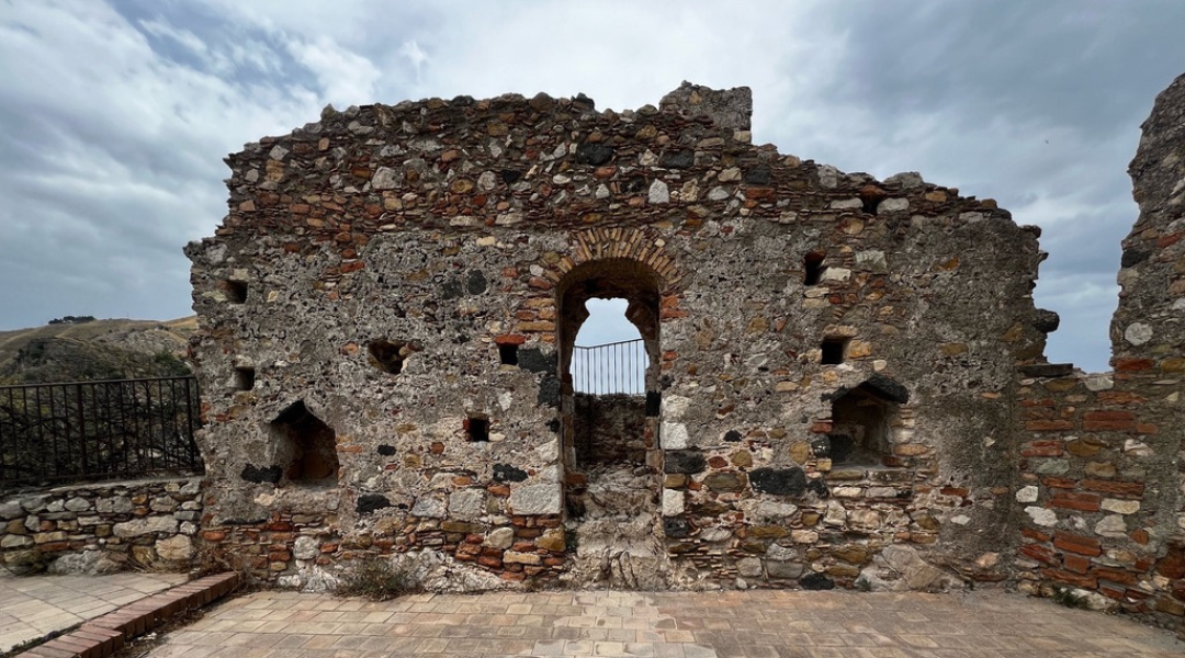 Ancient stone ruins with an arched doorway overlooking the sky in Sicily.