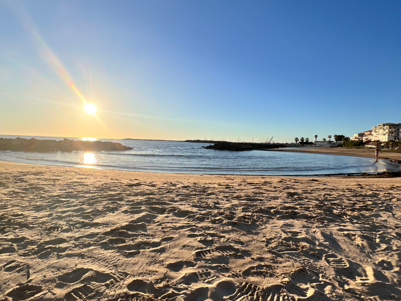 Sunset over the sandy beach in Scoglitti, Sicily, with calm waters and a clear sky.