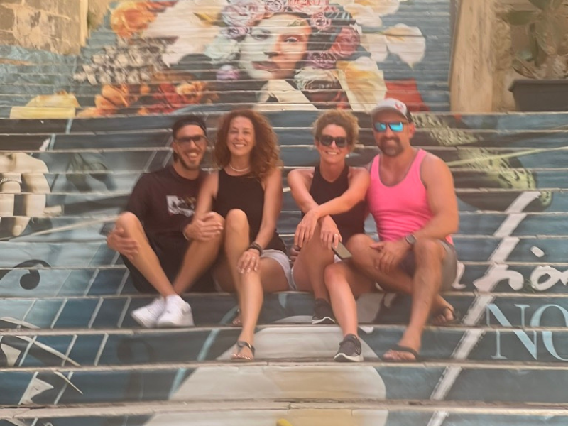 Monika, Alessio, and guests from tour group seated on the decorated steps in Noto, enjoying a vibrant day out.