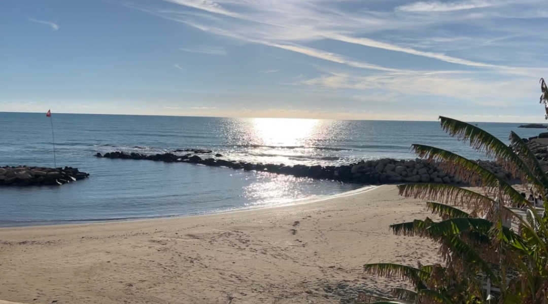 Calm beach in Scoglitti, Sicily, with the sun reflecting off the Mediterranean Sea and gentle waves lapping at the sandy shore.