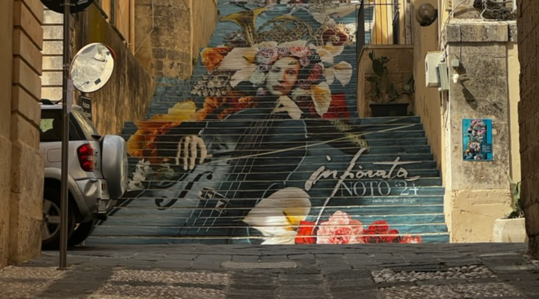 Colorful painted stairs in Noto, Sicily, featuring an intricate mural of a woman surrounded by flowers and musical elements.